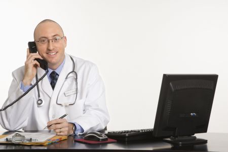 lekarz z telefonem przy biurku z komputerem